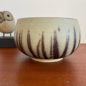 May include: A ceramic bowl with a light green glaze and brown brushstrokes. The bowl has a rounded shape and a slightly flared rim.