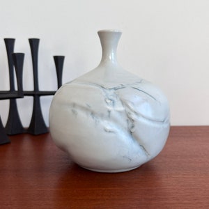 May include: A white ceramic vase with a marbled design. The vase has a round body and a narrow neck.