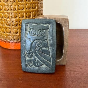 May include: A set of three ceramic mugs with a speckled, cream-colored glaze. Each mug features a different hand-painted floral design in shades of blue, green, and yellow. The mugs have a simple, rounded shape.