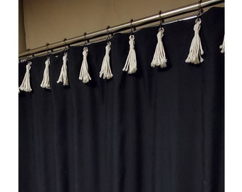 May include: Black shower curtain with white tassel trim. The curtain is hung on a silver shower rod.