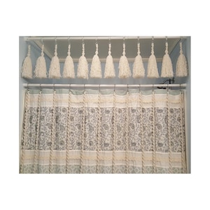 May include: A white shower curtain with a floral pattern and a white tassel valance. The valance is made of multiple strands of yarn with tassels at the end.