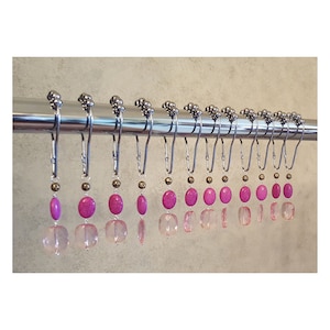 May include: A set of 12 shower curtain hooks with pink and clear glass beads. The hooks are silver and have a decorative design.