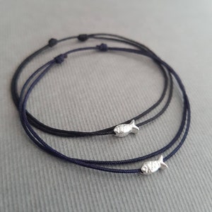 May include: Two black string bracelets with silver fish charms. The bracelets are layered on top of each other.