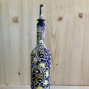 May include: A decorative dark blue glass bottle with a stainless steel spout. The bottle is adorned with a white and yellow paisley design. The bottle is approximately 12 inches tall.