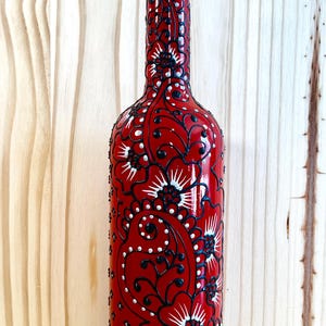 May include: A red decorative glass bottle with a black and white floral design. The bottle has a stainless steel spout and is suitable for olive oil or vinegar. The bottle is approximately 10 inches tall.