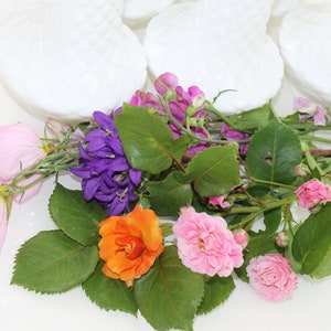 Puede incluir: Un ramo de flores rosas, moradas y naranjas con hojas verdes. Las flores est&aacute;n dispuestas en un cuenco blanco.