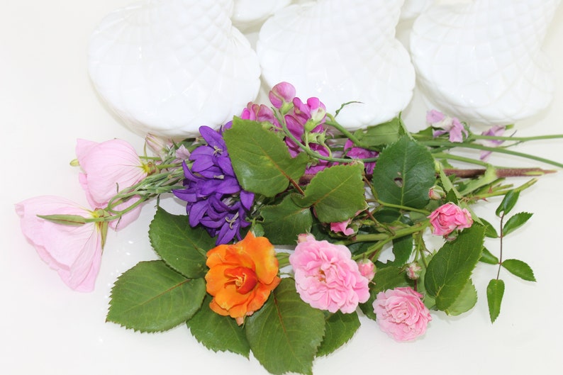 Puede incluir: Un ramo de flores rosas, moradas y naranjas con hojas verdes. Las flores est&aacute;n dispuestas en un cuenco blanco.