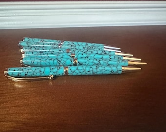 May include: A collection of four ballpoint pens featuring a bright turquoise barrel with a black crackle pattern. Each pen is accented with gold-toned metal components, including a pointed tip, a center band, and a curved pocket clip at the top.