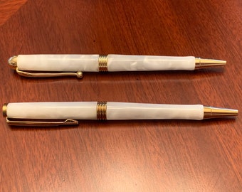 May include: Two white pens with gold accents. The pens have a marbled design and a gold clip.