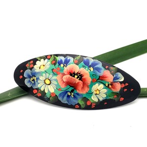 May include: Black oval hair clip with a hand-painted floral design. The design features red, pink, white, blue, and green flowers on a black background.