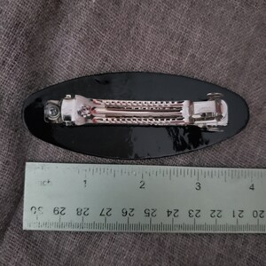 May include: Black oval hair clip with a silver metal clasp. The clip is approximately 2 inches long.