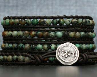 May include: A multi-layered leather bracelet with turquoise and brown beads and a silver charm with a tree design.