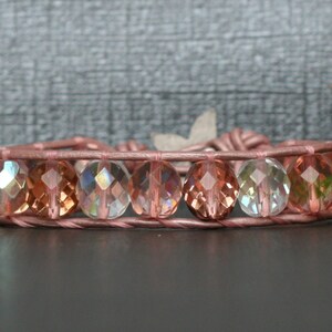 May include: A pink leather bracelet with iridescent faceted glass beads. The beads are a mix of clear, pink, and green.