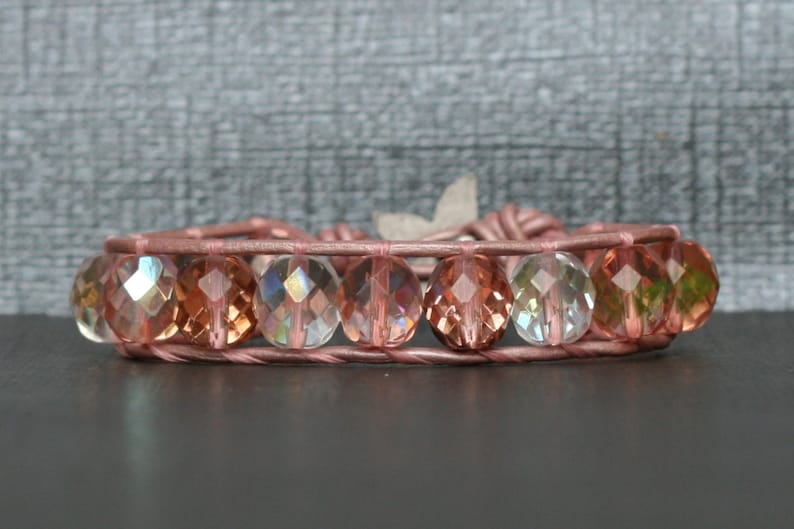 May include: A pink leather bracelet with iridescent faceted glass beads. The beads are a mix of clear, pink, and green.