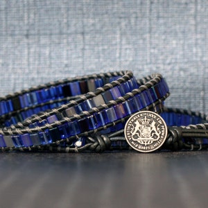 Puede incluir: Un brazalete de envoltura de cuentas azules y negras con un dije de moneda de plata que presenta un escudo de armas.