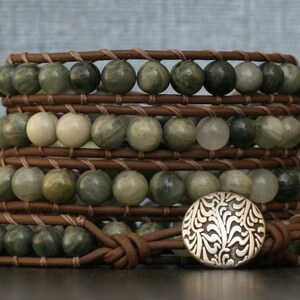 May include: A multi-layered leather wrap bracelet with green and white stone beads and a silver floral button closure.