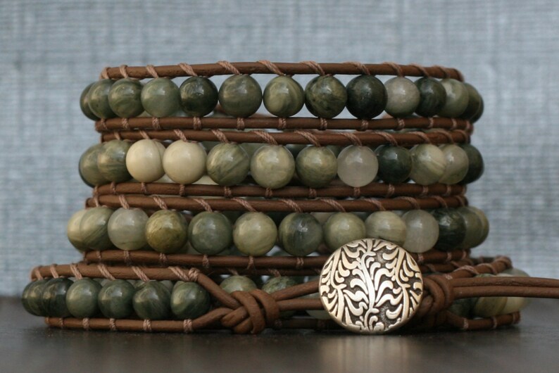 May include: A multi-layered leather wrap bracelet with green and white stone beads and a silver floral button closure.