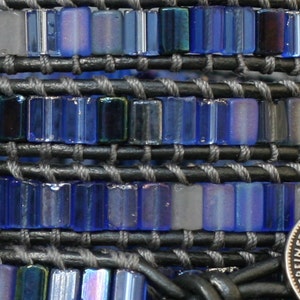 Puede incluir: Un primer plano de una pulsera de cuentas azules y grises con un dije de moneda de plata. La moneda tiene las palabras "Vereinsthaler" y un escudo de armas.