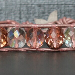May include: A pink leather wrap bracelet with iridescent faceted glass beads in shades of pink, clear, and green.