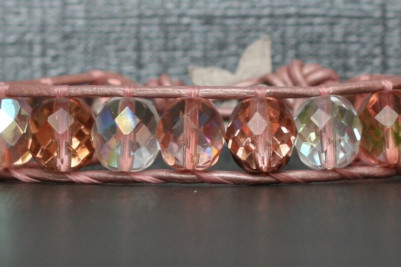 May include: A pink leather wrap bracelet with iridescent faceted glass beads in shades of pink, clear, and green.