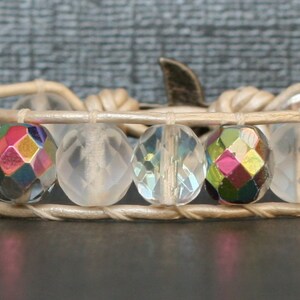 May include: A white leather bracelet with clear and iridescent faceted beads. The bracelet has a silver clasp.