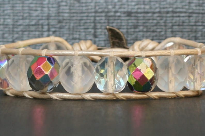 May include: A white leather bracelet with clear and iridescent faceted beads. The bracelet has a silver clasp.