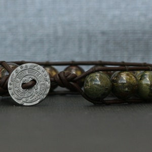 May include: A brown leather bracelet with a silver charm and green and brown stone beads.