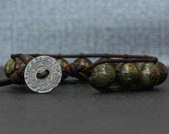 May include: A brown leather bracelet with a silver charm and green and brown stone beads.