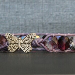 May include: A purple leather bracelet with a silver butterfly charm and faceted purple glass beads.
