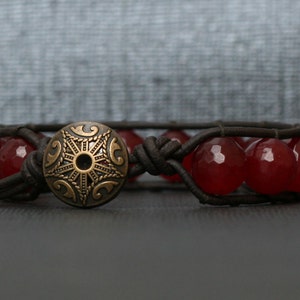 May include: A brown leather bracelet with red gemstone beads and a decorative metal clasp.