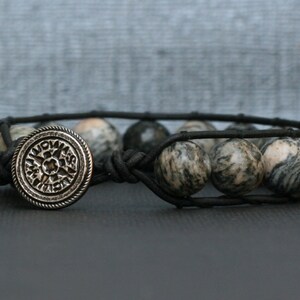 Peut inclure: Un bracelet en cuir noir avec un charme de boussole argenté et des perles marbrées grises et blanches.