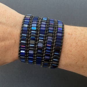 Puede incluir: Un brazalete de m&uacute;ltiples capas con cuentas de vidrio azul y negro iridiscentes y una base de cuero marr&oacute;n.