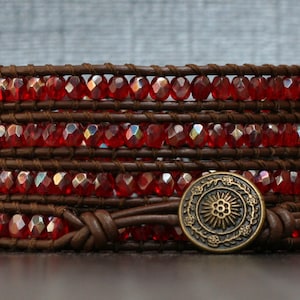 May include: A brown leather wrap bracelet with red crystal beads and a brass button closure.