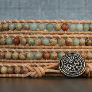 May include: A multi-layered leather wrap bracelet with brown leather straps and green, brown, and red gemstone beads. A silver charm with a star design is attached to the bracelet.