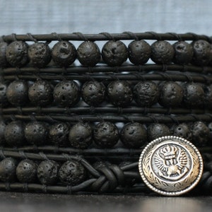 May include: A black leather wrap bracelet with multiple strands of black lava rock beads and a silver charm with a crown and wings.