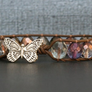 May include: A brown leather bracelet with a silver butterfly charm and iridescent glass beads.