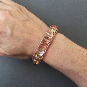 May include: A rose gold bracelet with iridescent glass beads.