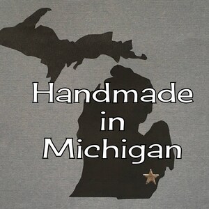 May include: Silhouette of the state of Michigan with the text "Handmade in Michigan" and a gold star.