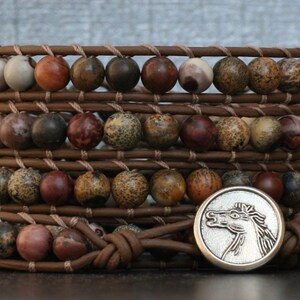 May include: A brown leather wrap bracelet with multiple strands of brown, red, and white jasper beads. A silver horse head charm is attached to the bracelet.