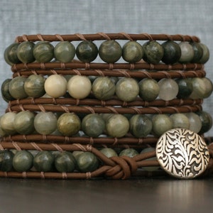 May include: A multi-strand leather wrap bracelet with green and white gemstone beads and a silver charm with a floral design.