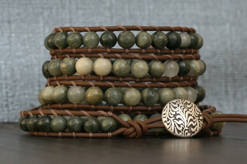 May include: A multi-strand leather wrap bracelet with green and white gemstone beads and a silver charm with a floral design.