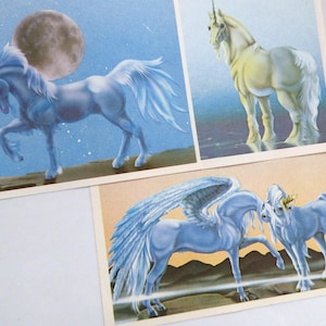 May include: Three fantasy art prints featuring unicorns. One print shows a blue unicorn with a horn and a star-like object in front of a moon. Another shows a white unicorn. The third print shows two unicorns with wings.