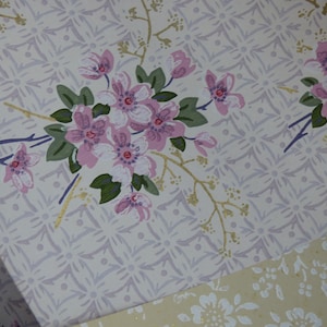 May include: Close-up of vintage wallpaper featuring a repeating geometric pattern in light gray. Pink floral bouquets with green leaves and gold accents are scattered across the surface, creating a delicate, feminine design.