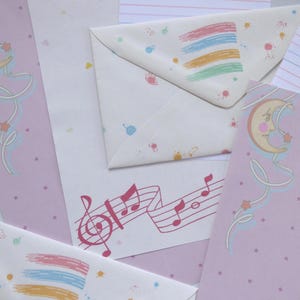 May include: Stationery set featuring envelopes and paper with whimsical designs. The envelopes have colorful brushstroke patterns and scattered dots. The paper includes musical notes, crescent moons, and stars in soft pastel colors, creating a dreamy aesthetic.