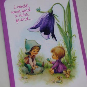 May include: A greeting card with a purple flower and two children. The card has the text "I could never find a nicer friend..."