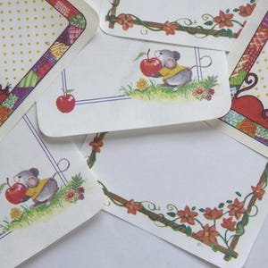 May include: A collection of stationery featuring a charming mouse illustration holding a red apple. The stationery has decorative borders with floral and patchwork designs, and a polka dot pattern.