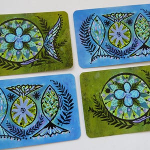 May include: Set of four rectangular coasters with a retro design. Two coasters have a green background, and two have a blue background. Each coaster features a stylized fish and floral design in shades of blue, green, and purple.