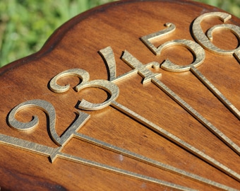 May include: A wooden plaque with gold-painted numbers 2, 3, 4, 5, and 6. The numbers are arranged in a fan shape.