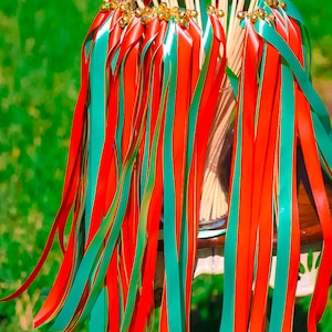 May include: A bunch of red and teal ribbon wands with gold bells at the top. The wands are tied together and are sitting on a white chair.