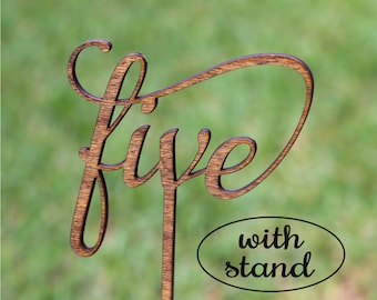 May include: Wooden table number with the word "five" in a cursive font. The number is attached to a wooden stand. The text "with stand" is printed in black on a white oval.